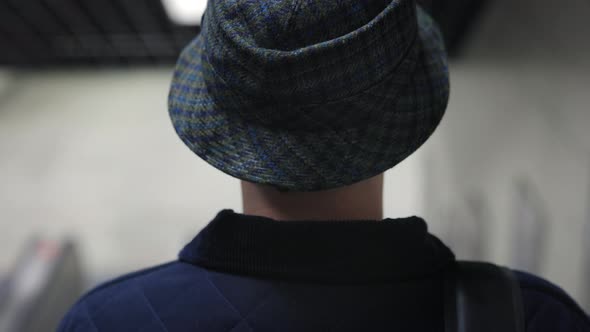Back View of Stylish Man in Bucket Hat Riding Down Escalator alt