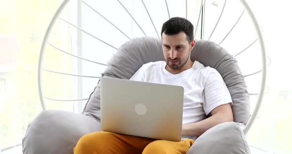 Young attractive man sitting on sofa at home working on laptop online.