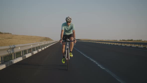 Slowmotion Video of a Male Cyclist Riding Along a Highway Behind a Camera Filming Him alt