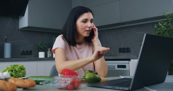 Woman Preparing Dinner for Her Family in the Kitchen and is Distracted on Phone  alt