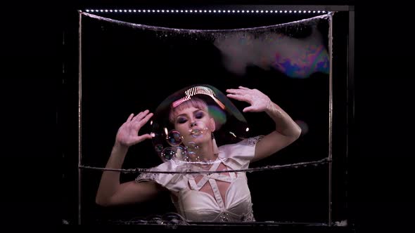 Beautiful girl does tricks with soap bubbles. She blows them out on the soap wall alt