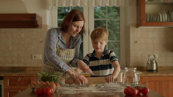 Young Mother Helping Her Cute Son Rolling Dough Standing in the Kitchen alt