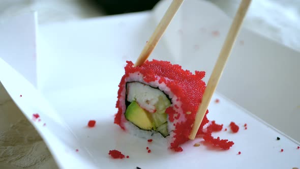 Lonely Sushi Roll in Tobiko Caviar is Taken with Wooden Chopsticks