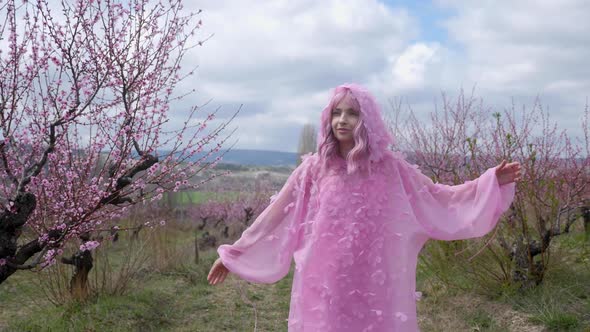 Woman in a Pink Hooded Dress with Flowers Walks Through a Peach Field alt