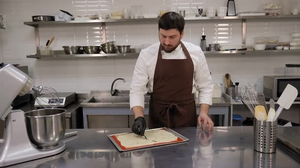 A Pastry Chef Man Spreading the Dough in a Baking Dish with a Spatula alt