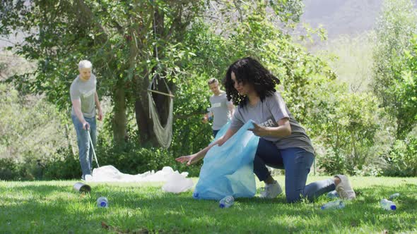 Happy diverse group of friends in volunteer t shirts putting plastic waste in refuse sacks outdoors alt