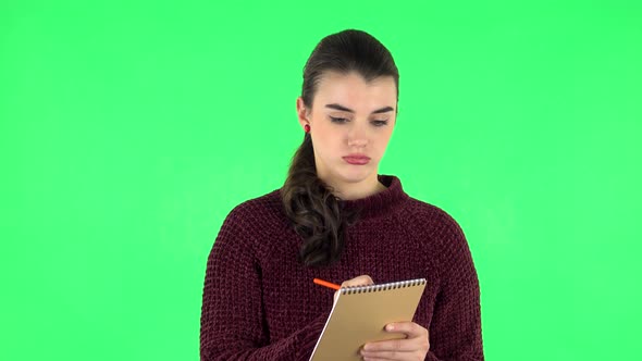 Girl Stands and Thinks, Then an Idea Comes To Her and She Writes with Pencil in Notebook. Green alt