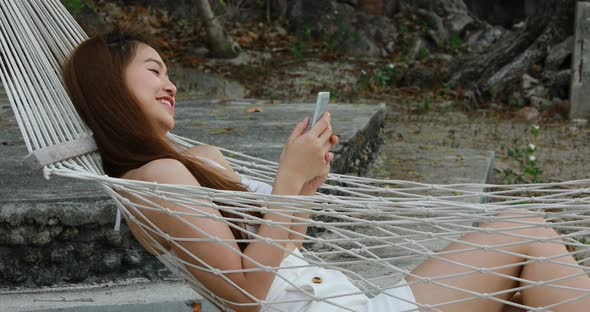 Summer Vacation of happy Asian woman wearing white bikini using mobile phone alt