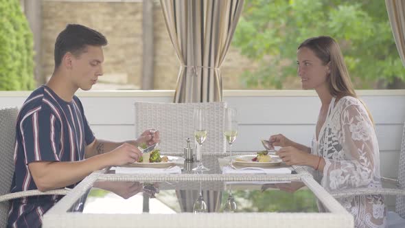 Side View Portrait of Happy Tourists Eating Delicatessen in Outdoor Restaurant and Talking. Young alt