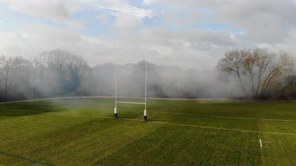 Drone Shot Of Rugby Pitch With Smoke Blowing Across, English Countryside, Cloudy Blue Sky