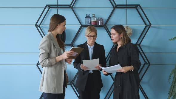 Three women stand against the wall in the office and check documents for a business project alt