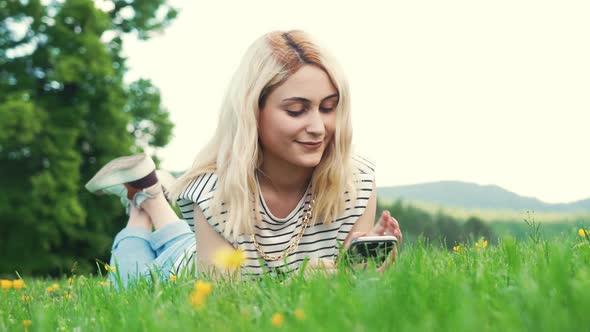 Young European Girl Lying on the Grass and Typing in Her Phone alt