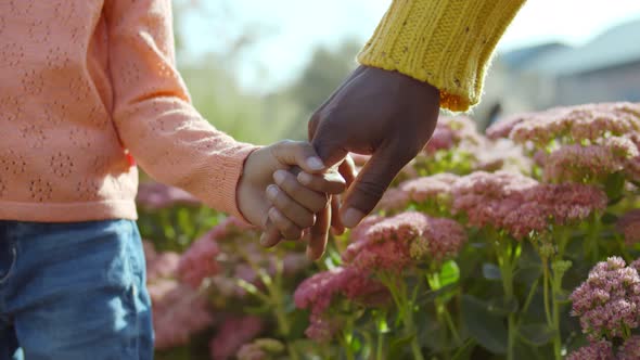 Close Up of African Father and Mixed Race Child Holding Hands Over Flower Bush Background alt