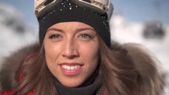 Portrait of a woman smiling lifestyle in the snow at a ski resort with goggles and beanie hat alt