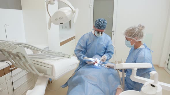 Two Professional Doctors Doing Dental Surgery Installing Dental Implants Into Patient's Mouth
