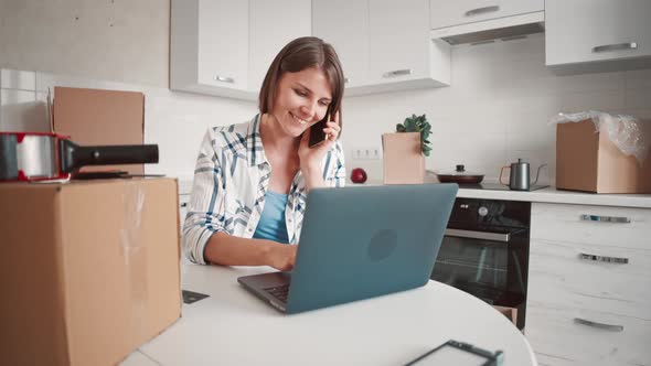 Female Talking By Phone Typing on Computer in Kitchen