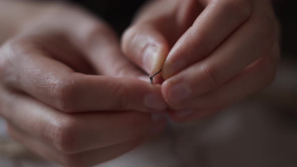 Close-up view of female hands inserting a thread into a needle hole for sewing. Handmade needlework. alt