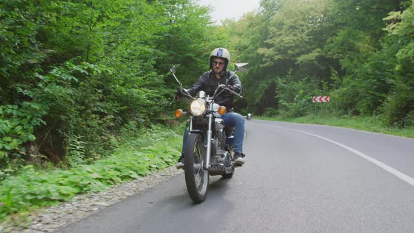 Young man riding a motorcycle on a forest road alt