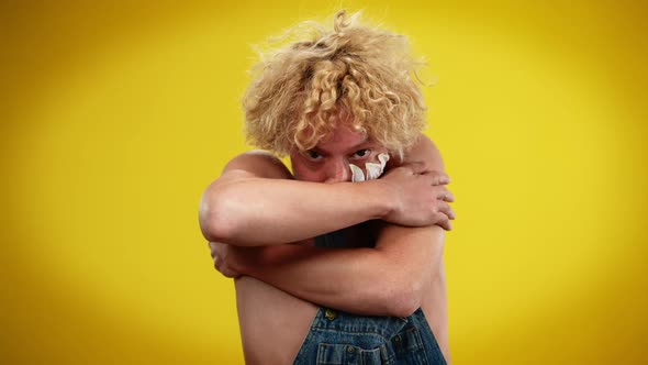 Portrait of Male Queer Person Hugging Himself Posing at Yellow Background alt