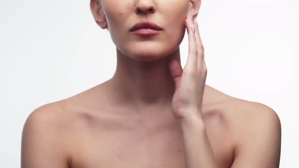 Woman Runs Finger Along Chin After Using Cosmetic Cream While Standing on White Background in Studio alt