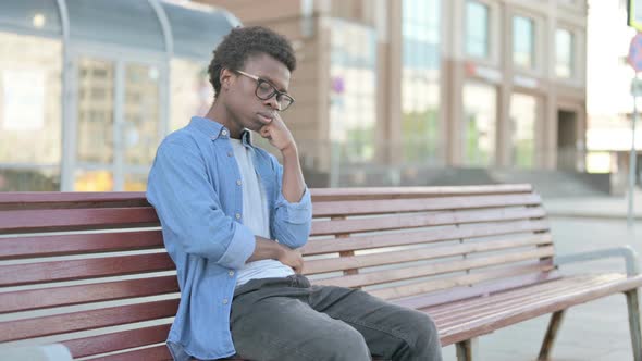 Tired Young African Man Sleeping While Sitting Outdoor on Bench alt