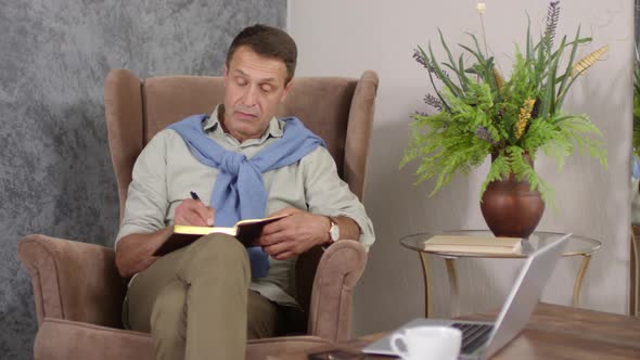 Middle-Aged Relaxed Caucasian Man Writing in Journal at Home alt