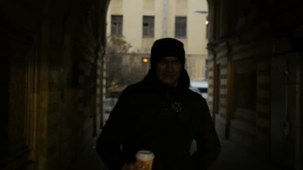 Front View Of Young Man Walking Down The City Street And Drinking Coffee To Go