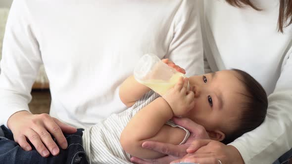 Asian Family of Young Father and Mother Feeding a Baby Boy From Milk Bottle alt