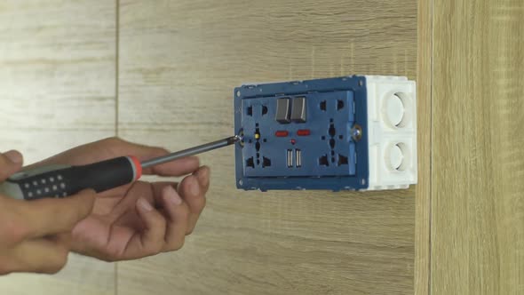 unscrew the screws from the socket in a plastic box on a wooden wall. alt