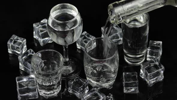 Pouring Up Shots of Vodka From a Bottle Into Drinking Glass. Black Background alt