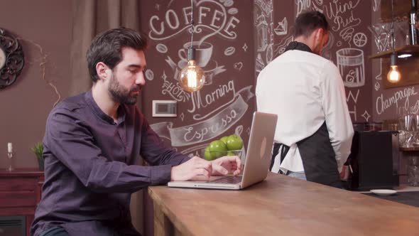 Young Man Working on His Laptop at a Bar Counter alt