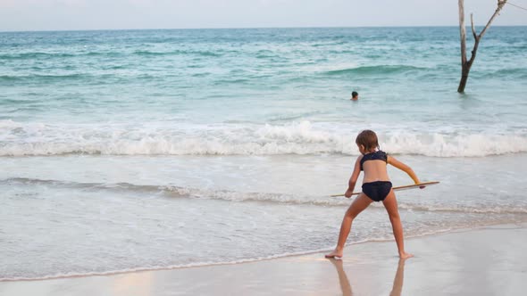 A Child Rides a Skimboard on the Coast of an Island in the Tropics alt