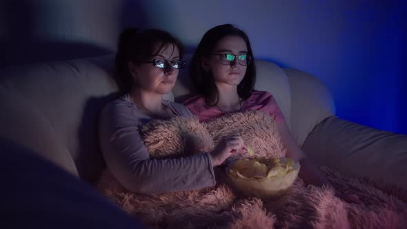 Mom and Daughter Watch Tv at Home in the Evening and Eat Chips