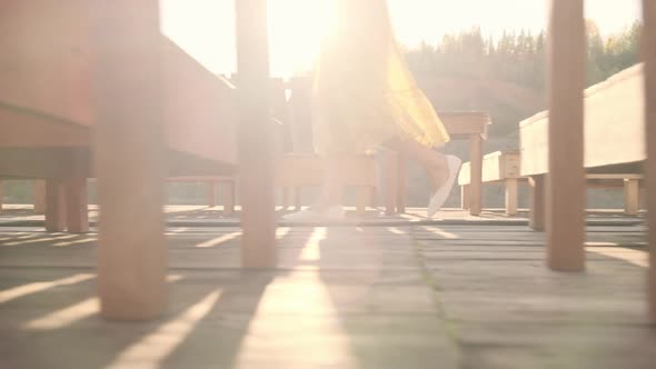 A young girl in a yellow dress walks alone along a wooden pier.