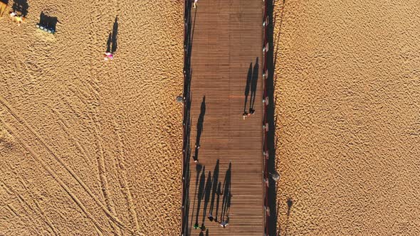 Fly Over Scenic Beach With People Walking On Pier alt
