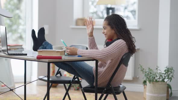 Wide Shot of Relaxed Teenage African American Girl with Feet on Table Surfing Social Media on alt