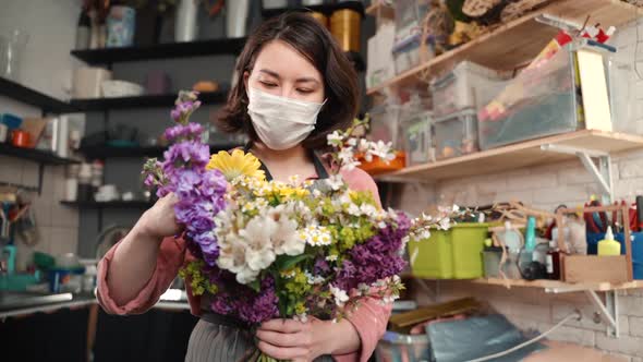 Woman in Fasial Protective Mask Fixing Flowers. Young Female Florist Composes a Bouquet of Chamomile