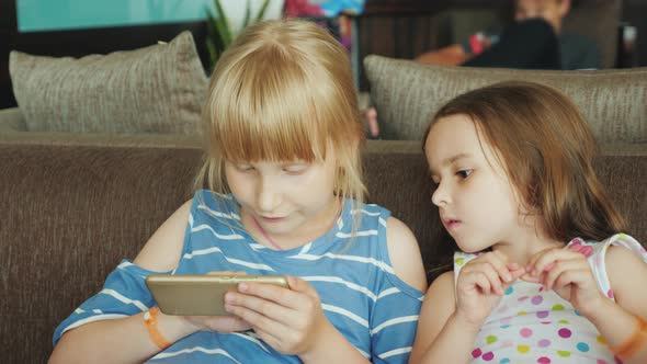 Little Sisters Rest on the Sofas at a Tourist Hotel on the Retsepshina Play Games on the Mobile alt