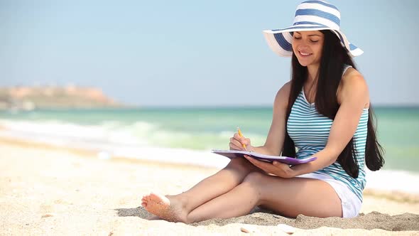 Young female student lying on sand with note and book on the beach