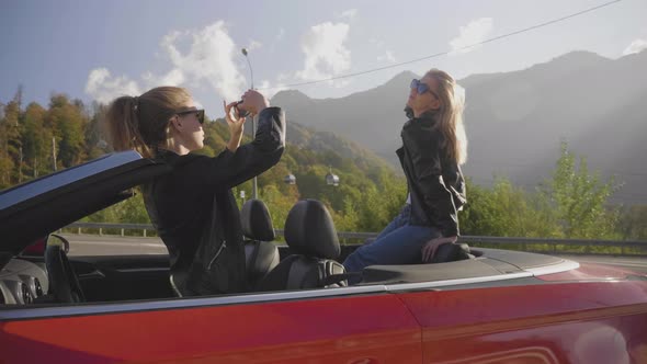 Beautiful Girls Take Photos on a Smartphone Inside a Red Convertible