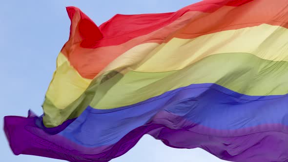 The rainbow flag, LGBT pride flag gay pride flag waving in the wind blue sky close up 4k alt