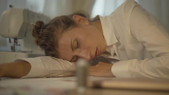 Close-up Portrait of Exhausted Young Caucasian Woman Sleeping on the Table with Sewing Machine at alt