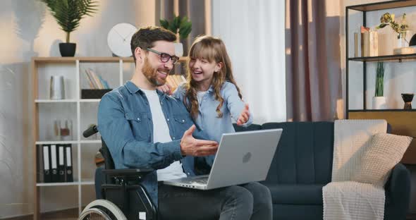 Disabled Dad in Wheelchair Having fun Together with His 10-aged Daughter while Using Computer alt