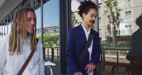 Two diverse male friends walking together wheeling bicycles in street alt