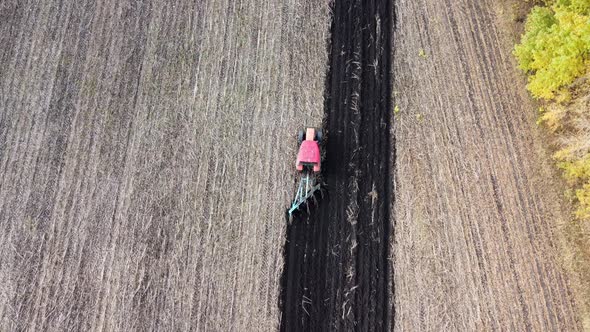 Shooting From Drone Flying Over Tractor with Harrow System Plowing Ground on Cultivated Farm Field