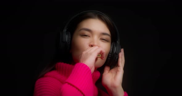 Woman Listens to Music in Wireless Headphones Smokes Vape on a Black Background alt