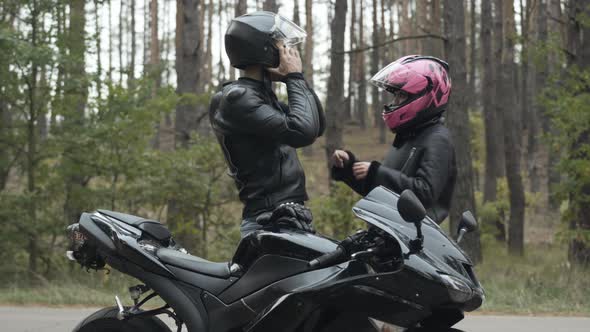 Side View of Confident Motorbiker Putting on Helmet and Loving Girlfriend Fastening It. Young alt