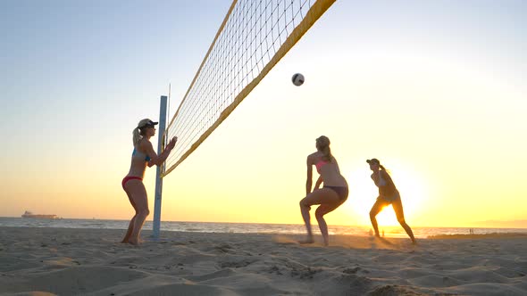 Women players play beach volleyball and a player hitting spiking the ball. alt
