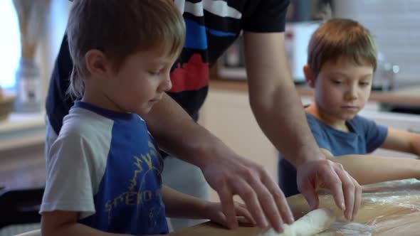 father showing children how to roll dough. alt