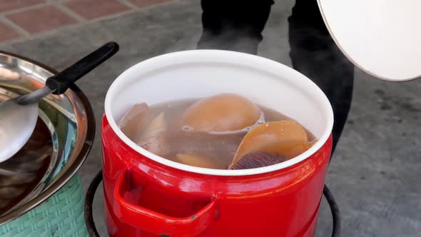 Woman hand opens the lid at the red pan with boiled Giant Sea Snail alt